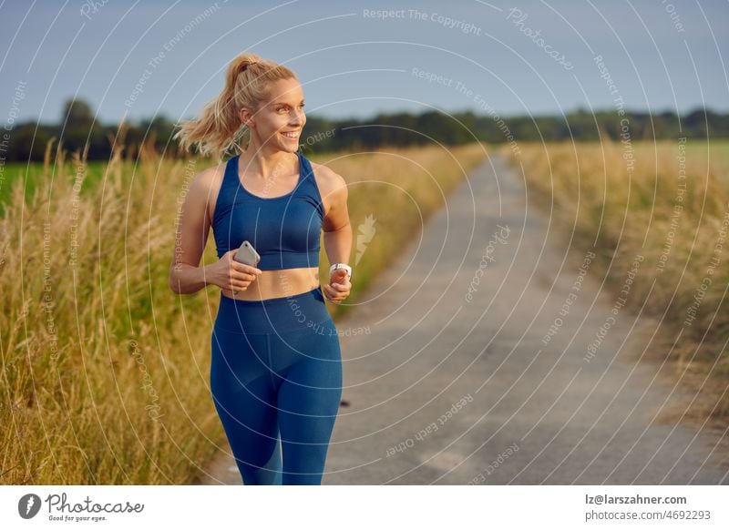 Fit healthy young woman enjoying a jog along a country road passing the camera with a happy smile full of vitality in an active lifestyle concept fit blond