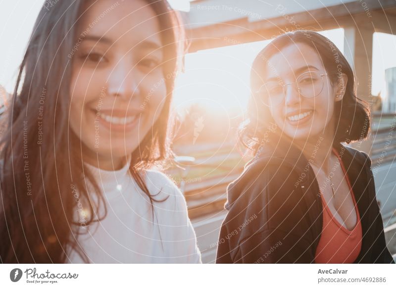 Two young woman friends sitting outdoors during a colorful sunset resting from workout. Training losing weight with friends together smiling to camera happy. Friendship between sisters concept