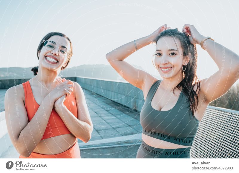Two woman tying up their hair before starting running jogging outdoors on urban place. Training losing weight with friends together smiling to camera happy. African arab people doing exercise.