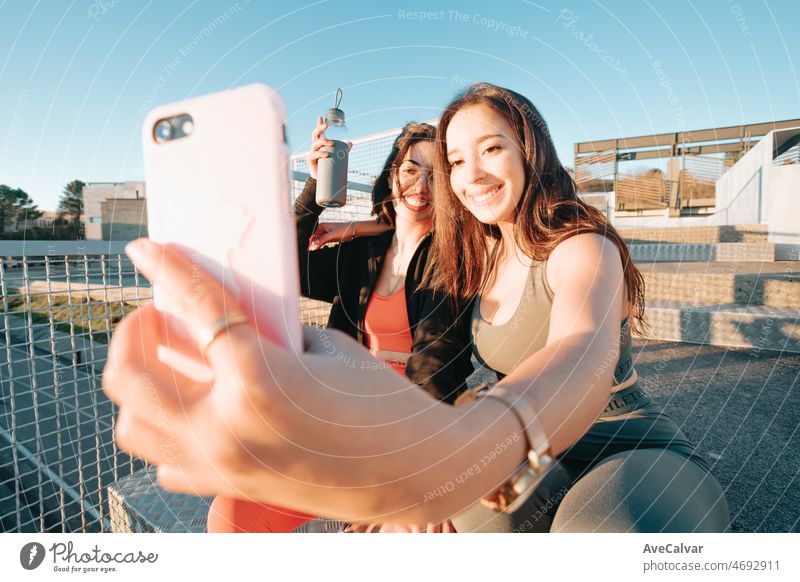 Two young sporty woman friends taking selfies with smart phone between exercises to show off on social media . Training losing weight with friends together smiling to camera happy. Sisters concept