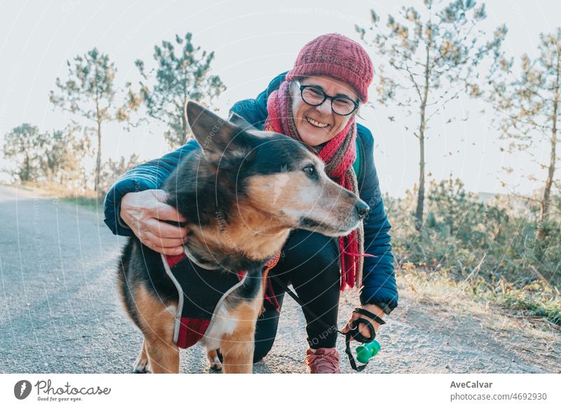 Old woman with his dog during a walk portrait wearing a hat for spring and winter smiling toc amera. Senior people mental health activities outdoors, Active lifestyle on third age. Happy grandma
