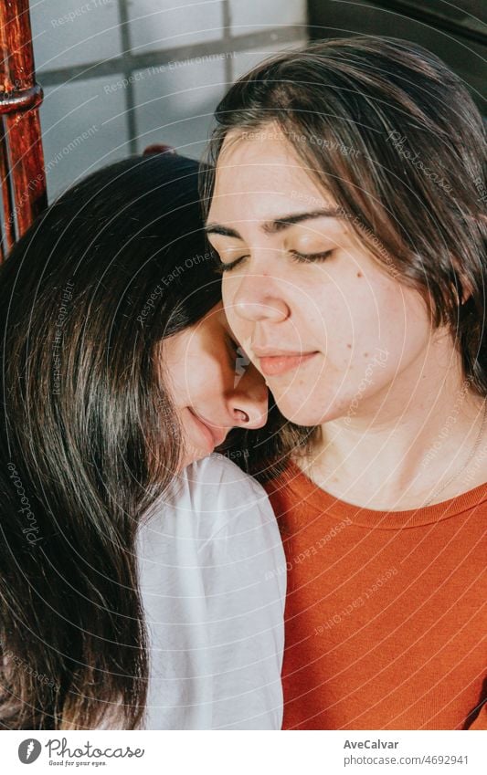 Close up portrait young and modern lesbian couple cuddling and smiling to each other while sitting on a modern chair on a gallery on a flat.Happy together. LGBTI+ love.Pride and right fighting concept