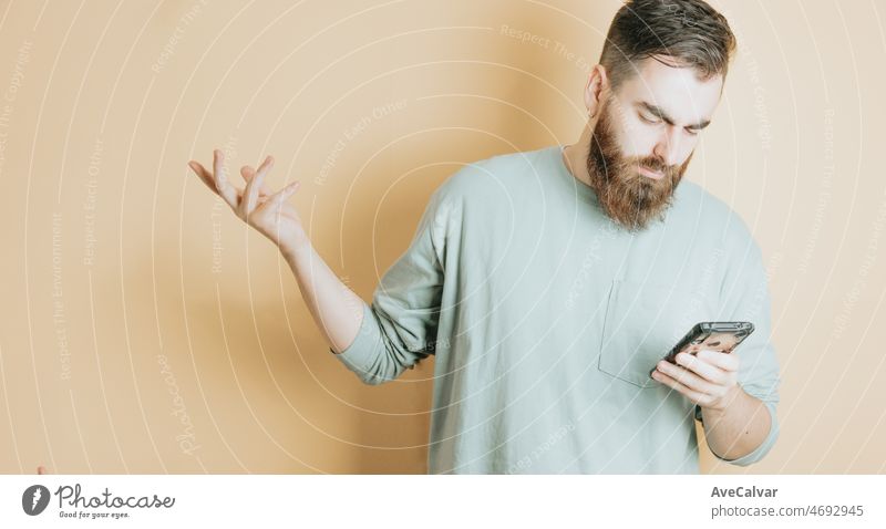 Young man bearded hipster style reading phone worried about a new, yellow background. Emotion about receiving a good new, removable background with copy space. Young people social network