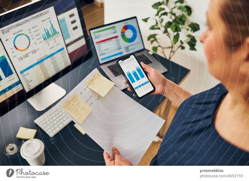 Businesswoman working with financial data on charts and tables on smartphone and computer. Woman entrepreneur looking at sale stats business office graph