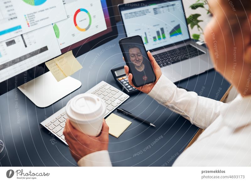 Woman entrepreneur having business video chat on smartphone. Businesswoman working with data on charts, graphs and diagrams on computer screen call colleague