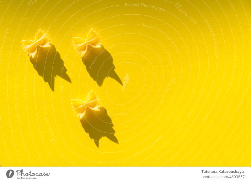 Three pieces of farfalle paste on a yellow background food uncooked raw pasta three italian ingredient diet italy nutrition wheat healthy traditional culinary