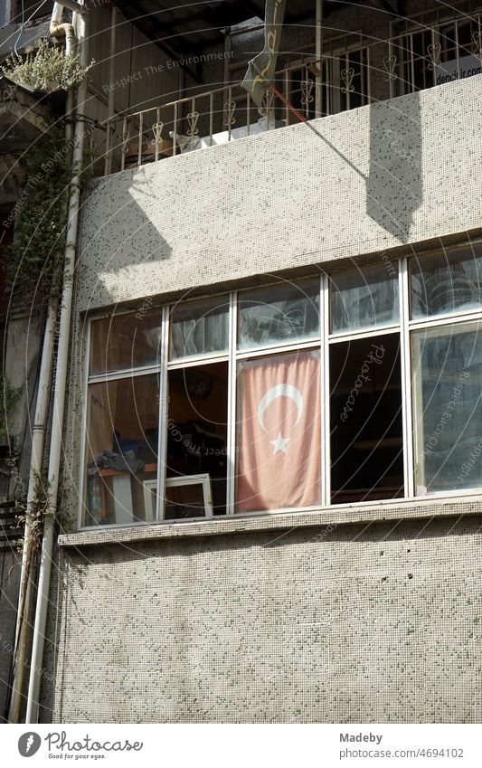 Yellowed red Turkish flag in the window of a run-down office in summer sunshine in the alleys of the old town of Taksim on Istiklal Caddesi in the Beyoglu district of Istanbul on the Bosphorus in Turkey