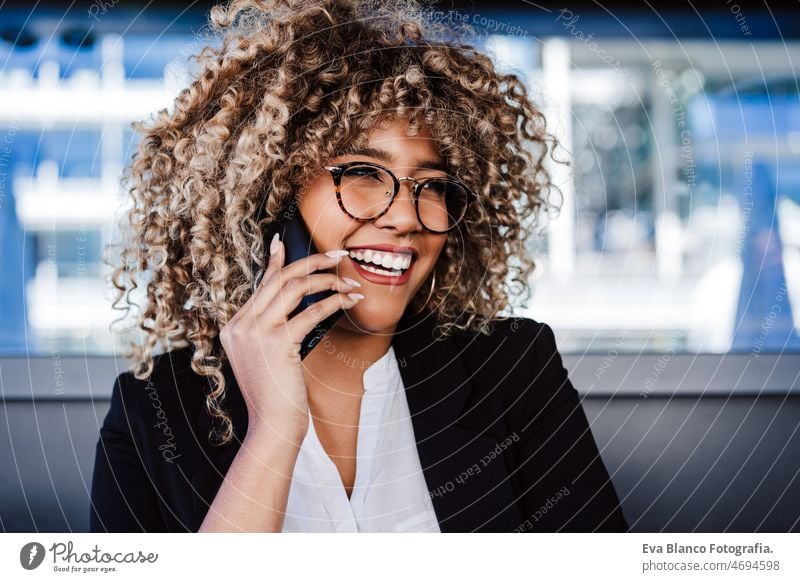 smiling hispanic afro business woman wearing eye glasses in cafe using laptop and mobile phone computer working networking drinking coffee terrace outdoors