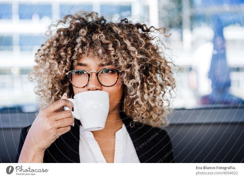 beautiful hispanic afro business wearing eye glasses drinking coffee in cafeteria. business concept woman laptop working networking terrace outdoors goggles