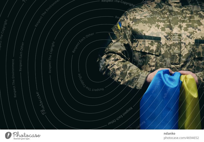 soldier of the Ukrainian armed forces stands with a blue-yellow flag of Ukraine on a black background adult ammunition army camouflage caucasian clothing combat