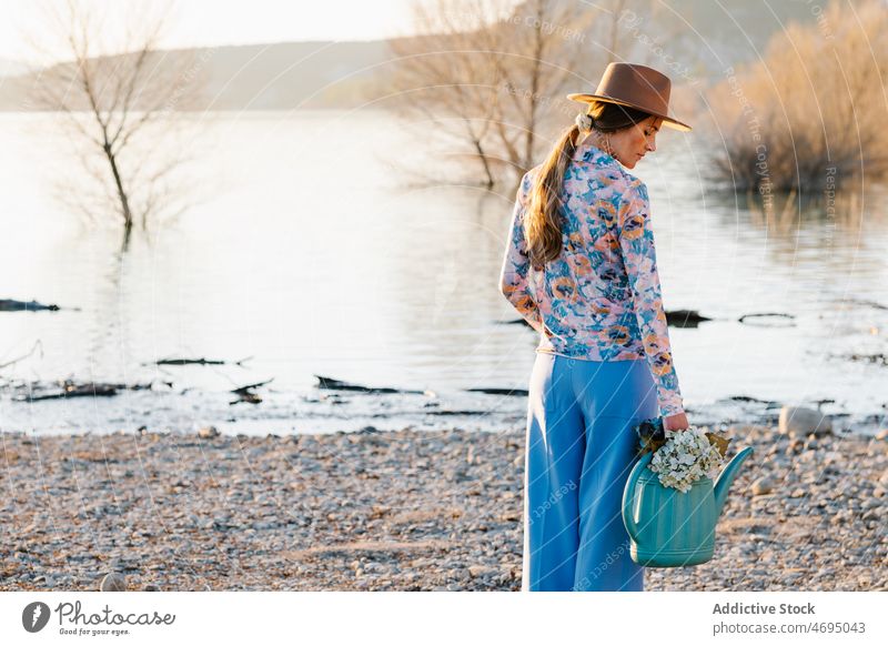 Woman with watering can with flowers on shore woman beach style river nature feminine riverside appearance hat bloom summer spring countryside coast female