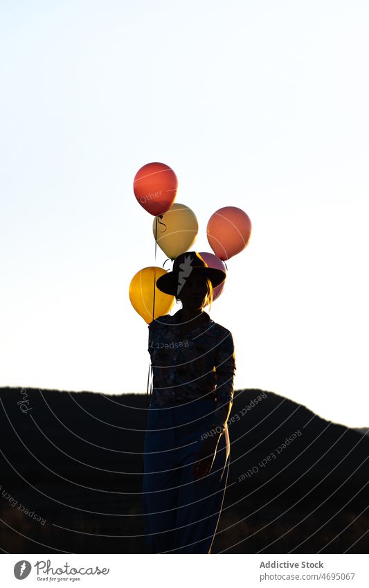Anonymous woman with balloons in countryside silhouette sunset nature evening shadow festive pastime leisure mountain sundown colorful ridge cloudless female