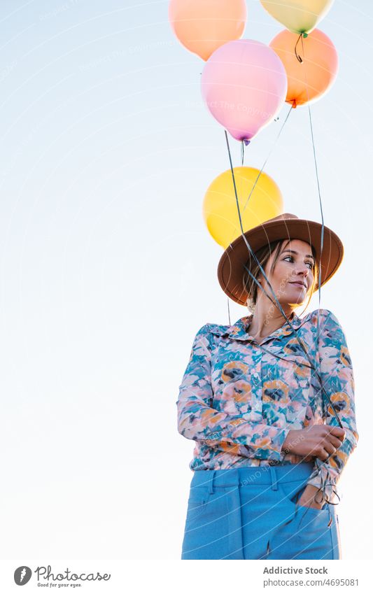 Pensive woman with balloons against cloudless sky countryside nature style female hat colorful thoughtful summer bright dreamy outfit waterfront range leisure