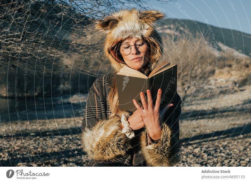 Lady in fur fox cap with book on lake shore woman read hat river coast style stone fluff water female natural headwear pastime headgear waterfront animal