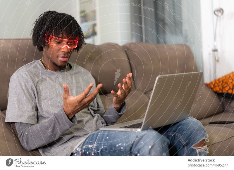 Black man in futuristic glasses looking at hands cyberpunk future high tech trendy modern laptop living room light male black african american couch sofa