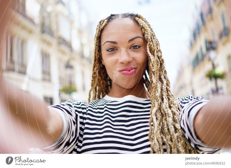 Black woman with afro braids taking a selfie in an urban street with a smartphone. portrait black afrobraid dreadlocks happy happiness african hairstyle girl