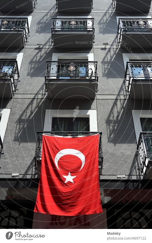 Bright red Turkish flag on the balcony of a beautiful residential building with gray facade in the summer sunshine in the Galata neighborhood in the Beyoglu district of Istanbul on the Bosphorus in Turkey