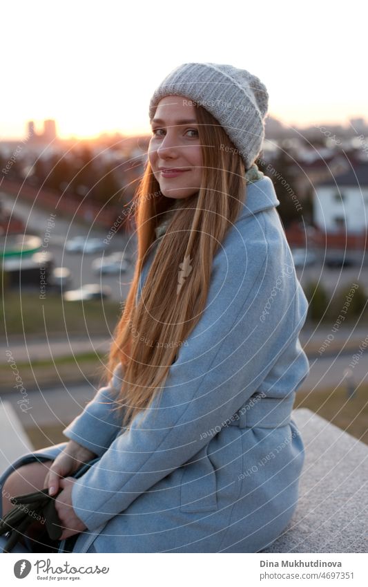 Woman in stylish blue coat at sunset. Female travel. Beautiful attractive young woman walking on the street at sunset or sunrise early in the morning near modern architecture buildings in the city. Casual candid lifestyle.