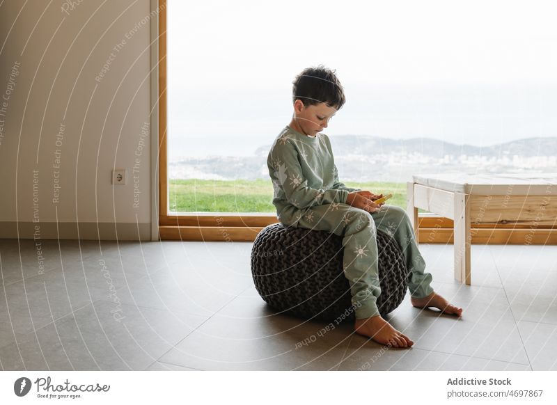 Boy in pajama playing on smartphone boy kid childhood videogame pastime morning domestic room apartment adorable barefoot flat cute home residential nightwear