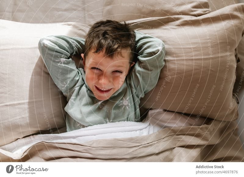 Cheerful boy lying down on bed kid window bedroom pajama childhood morning cheerful having fun funny apartment adorable flat delight cute home residential happy