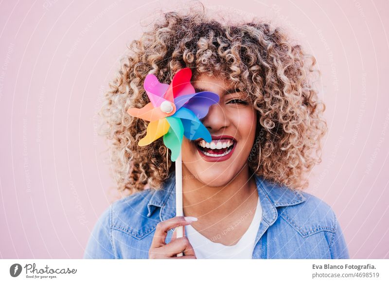 beautiful happy hispanic woman with afro hair holding colorful pinwheel. pink background,wind energy windmill sustainability reduce reused recycle city smiling