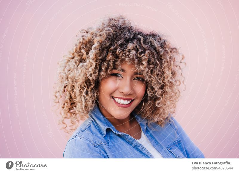 portrait of smiling hispanic woman with afro hair in city during spring. Urban lifestyle pink happy casual clothing curly hair outdoors urban adult laughing