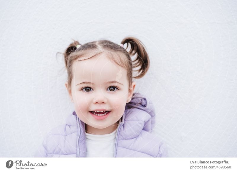 portrait of beautiful caucasian two year old baby girl smiling over white background. childhood outdoors city coat cold winter happy pony tail little small