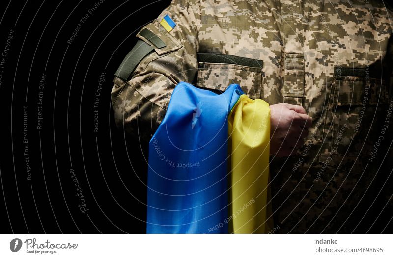 Ukrainian soldier holds a flag of the independent state of Ukraine. Steadfastness and courage of the people in the fight against the invaders. Unbroken spirit of the nation. Symbol of independence