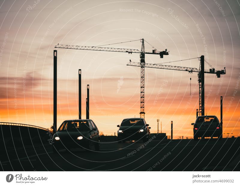 Construction cranes and road traffic at sunset Silhouette Sunlight Sunset Crane Sky Clouds Bridge car Car lights Back-light Traverse melancholy Play of colours