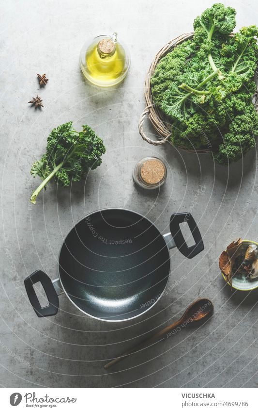 Food background  with cooking pot and green kale leaves empty wooden cooking spoon healthy ingredients raw olive oil star anise grey kitchen table home seasonal