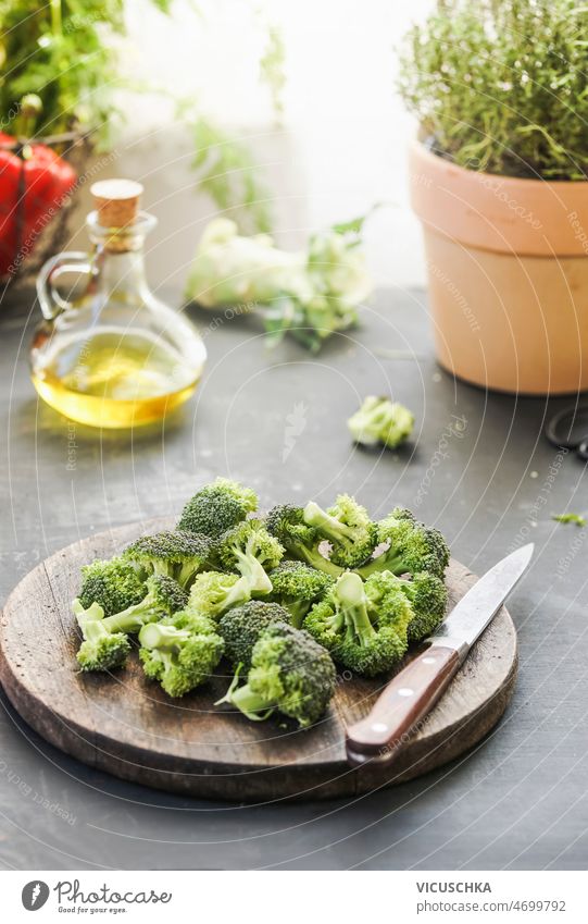 Broccoli at wooden cutting board with kitchen knife at grey kitchen table broccoli herbs oil ingredients background natural lights cooking home green vegetables