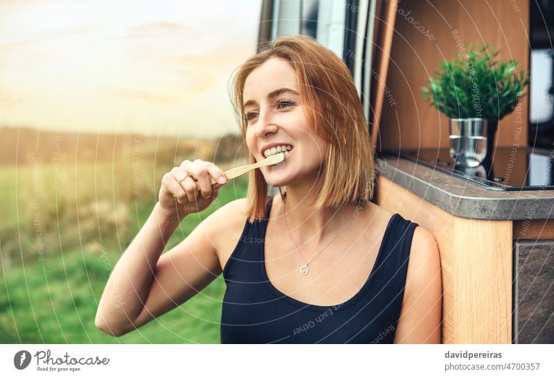 Woman brushing her teeth with a bamboo toothbrush outdoors young woman morning camper van trip smiling copy space health care clean cheerful dental female happy
