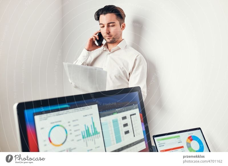 Man entrepreneur having business  conversation on mobile phone. Businessman holding documents and smartphone working with data on charts and graphs in office