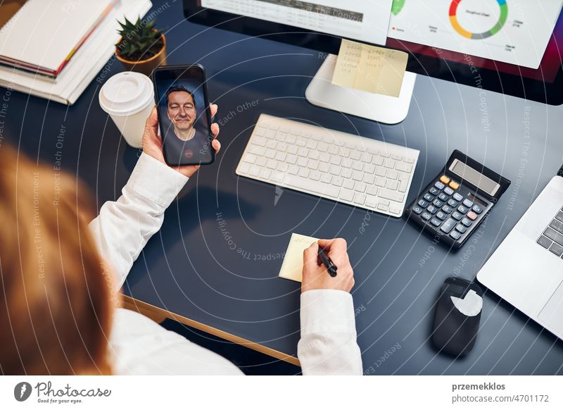 Woman entrepreneur having business video chat on smartphone. Businesswoman making notes while talking to her business partner call colleague conversation
