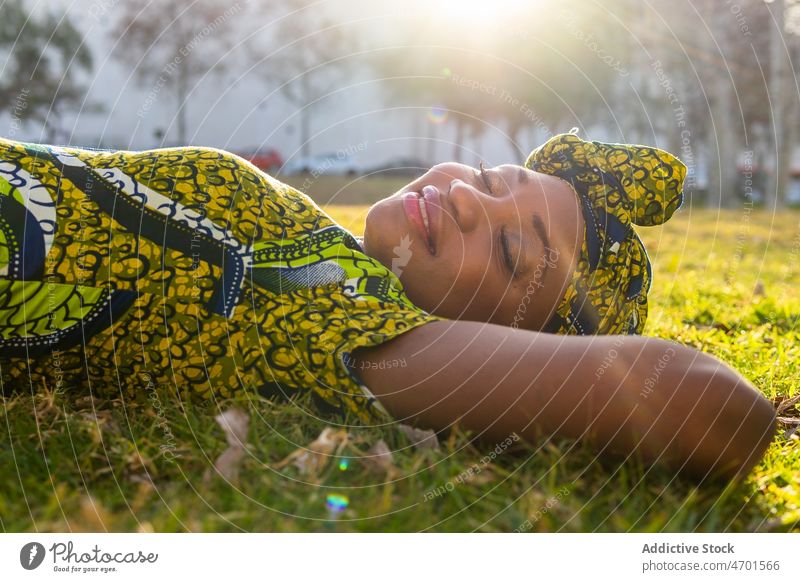 African woman resting on lawn park smile weekend summer glad grass daytime female tradition headscarf portrait african american black ethnic happy relax