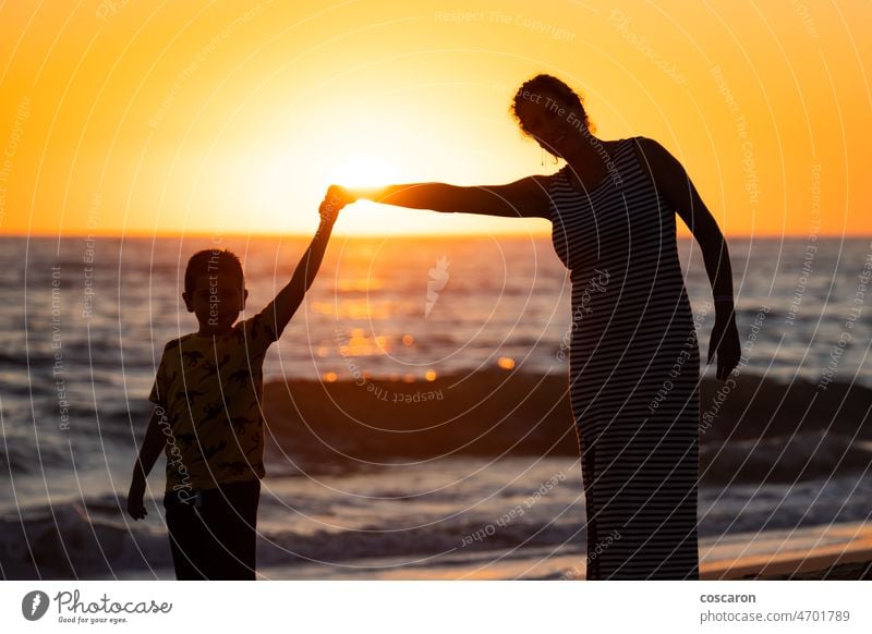 Mother and son holding hands on a beach at sunset baby cheerful child coast daughter enjoy enjoying family female fun girl happiness happy holiday holidays kid