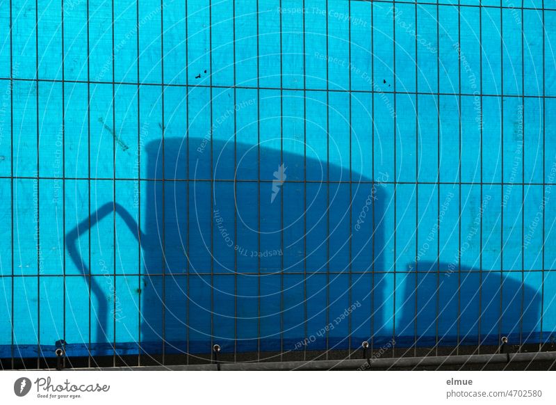 Shadow of different parts behind a metal fence covered with a blue plastic tarpaulin as a privacy screen / shadow play / barrier Shadow play Fence Metalware