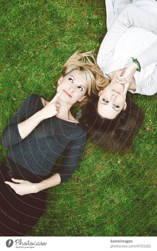 Two thoughtful girls lying in the grass women questioning day dreaming friends ask think beautiful background beauty blond brainstorming brunette caucasian