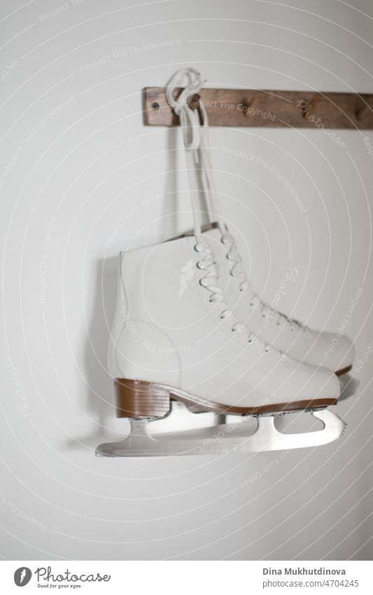 White ice skates hanging on white laces on a wooden hanger on white wall. Winter active sports figure ice skating equipment. leisure object activity season