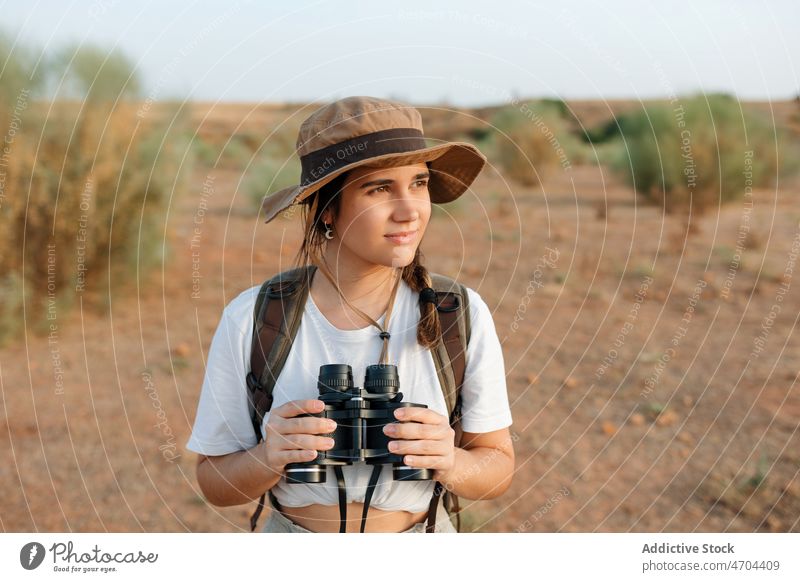 Woman with binoculars in desert field woman traveler trip adventure arid journey explore admire enjoy distance content glad optimist happy barren dry bush
