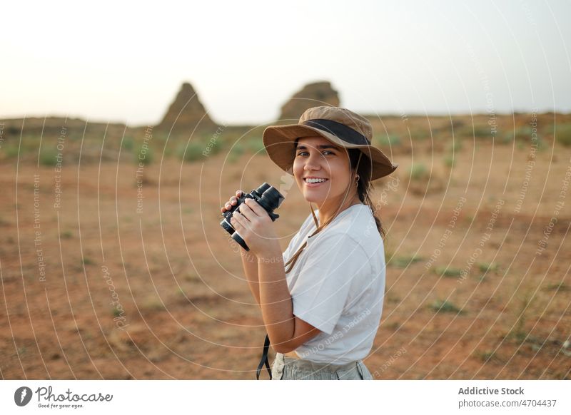Smiling woman looking through binoculars in desert area traveler trip adventure arid journey explore observe interest curious barren dry bush vegetation