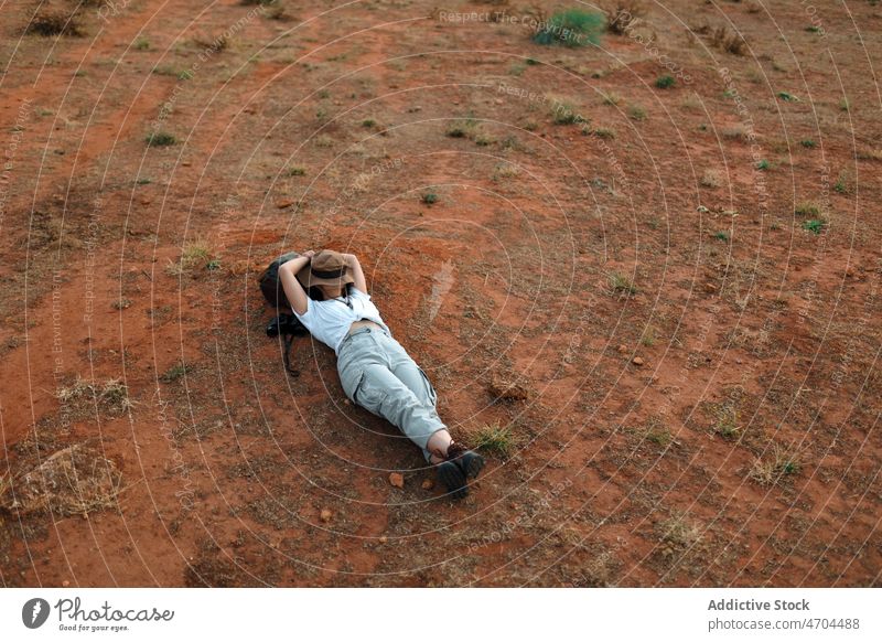 Relaxing woman lying on ground in desert traveler trip adventure arid journey explore barren dry waterless tourism tourist drought environment scene plant
