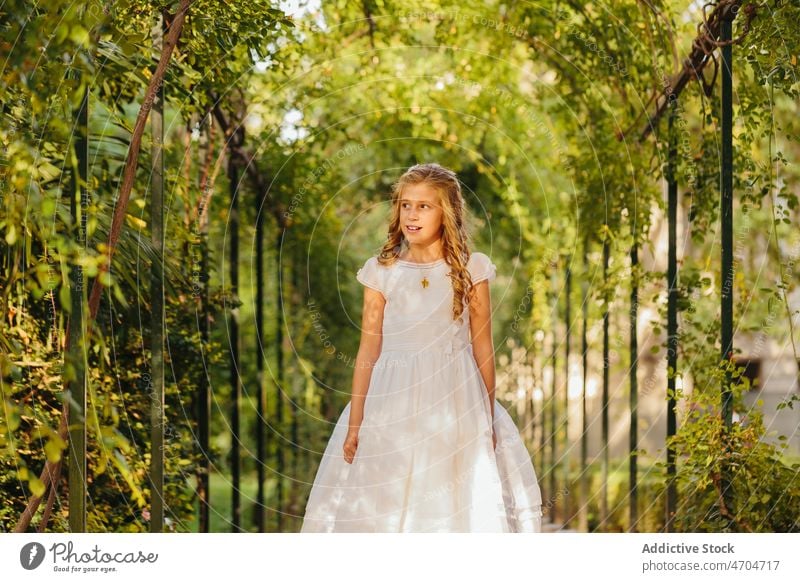 Charming girl in First Communion dress standing in park religion communion peaceful first communion catholic holy communion summer smile positive happy cheerful