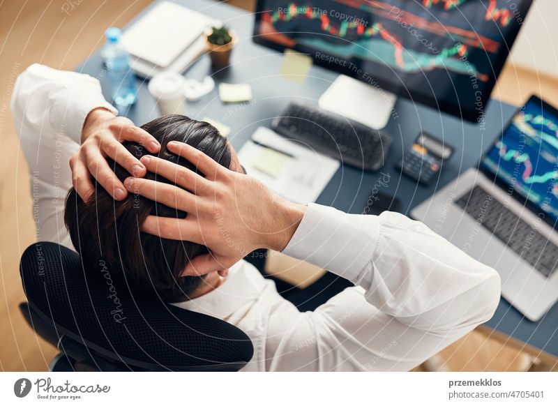 Worried businessman looking at charts stressed by news from stock market. Investor lost money online. Man analyses loss and profit. Businessman investing stocks online. Man working with stock chart data
