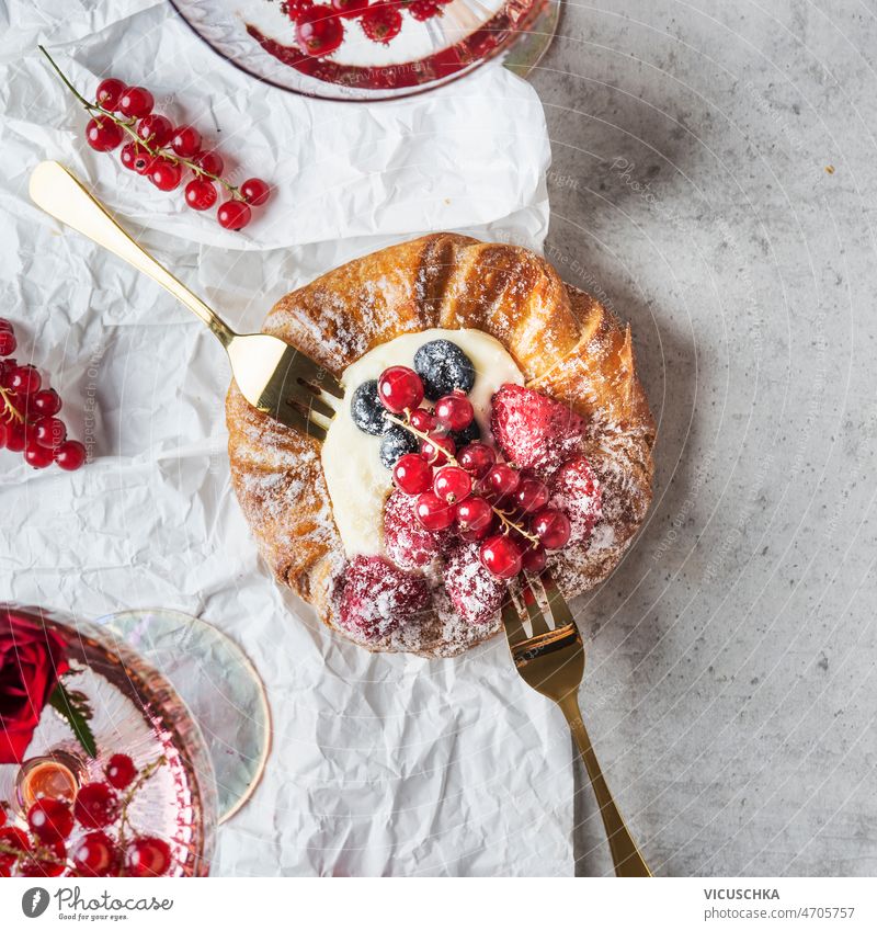 Close up of beautiful pastry with cream and berries close up raspberries red currants blueberries powdered sugar golden forks grey concrete table white paper