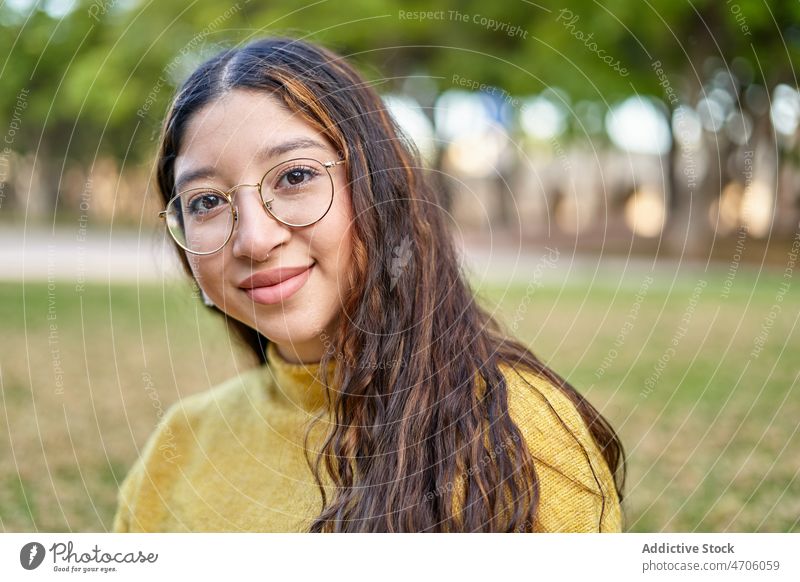 Positive woman sitting on lawn park feminine appearance style smile summer young tree eyeglasses lady pleasant plant long hair youth female beautiful charm