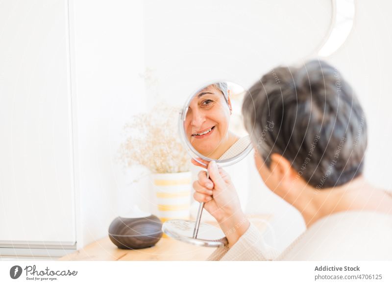 Woman looking at mirror in room woman reflection appearance skin care middle age domestic feminine daily routine bathrobe home content glad female short hair