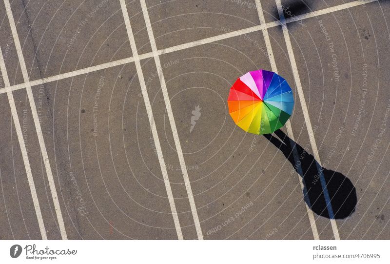 Aerial view of woman holding rainbow umbrella parking lot background - view from a drone top crossing color crosswalk abstract road city walking business cement