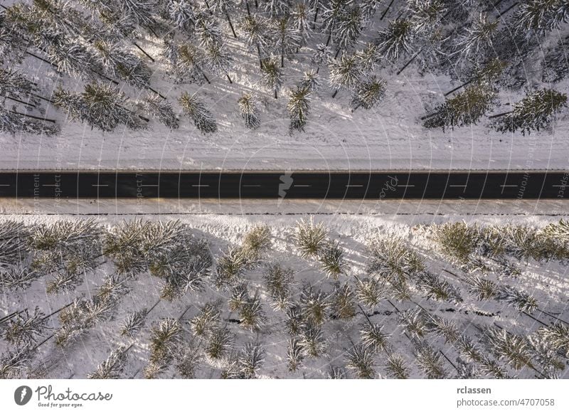 Aerial drone view of road in idyllic winter landscape at sunset. Street running through the nature from a birds eye view forest aerial snowy sunlight above