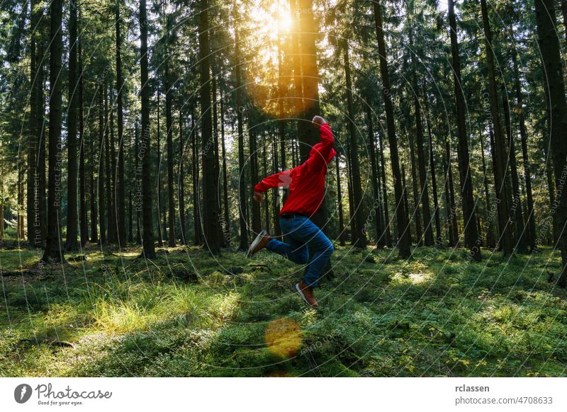 Young man jumps in the green forrest with red jacket and enjoys nature hiker explore forest silence autumn adventure analog spring summer run beautiful